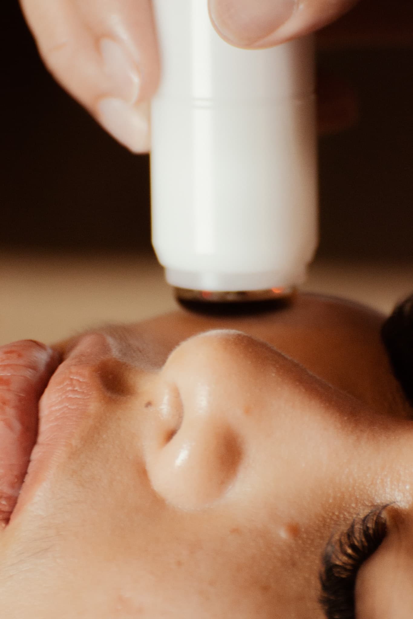 A Cryoskin facial wand held just above a client's face during a treatment.